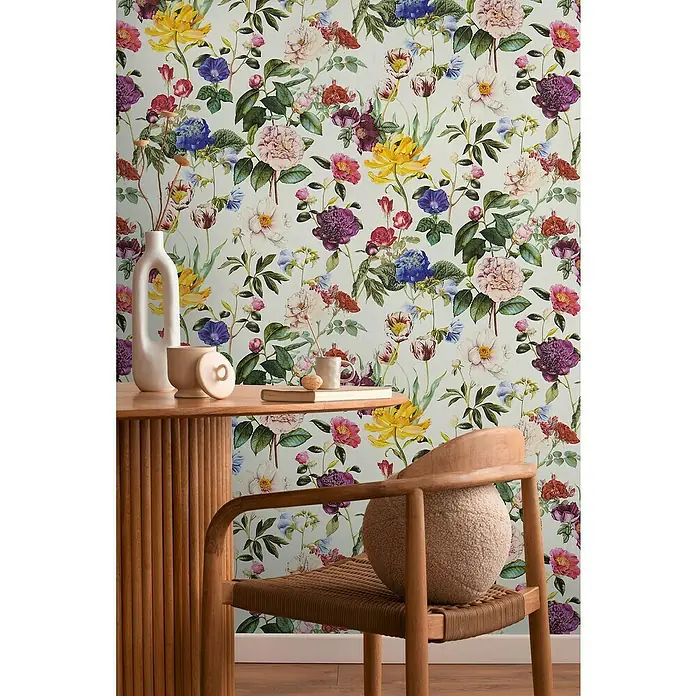A.S. Création Designdrop Vliestapete Blumen - Bunt, Floral, 10,05 x 0,53 m - Nahaufnahme eines Raumes mit floral gemusterter Tapete und einem Holztisch mit Deko-Elementen.