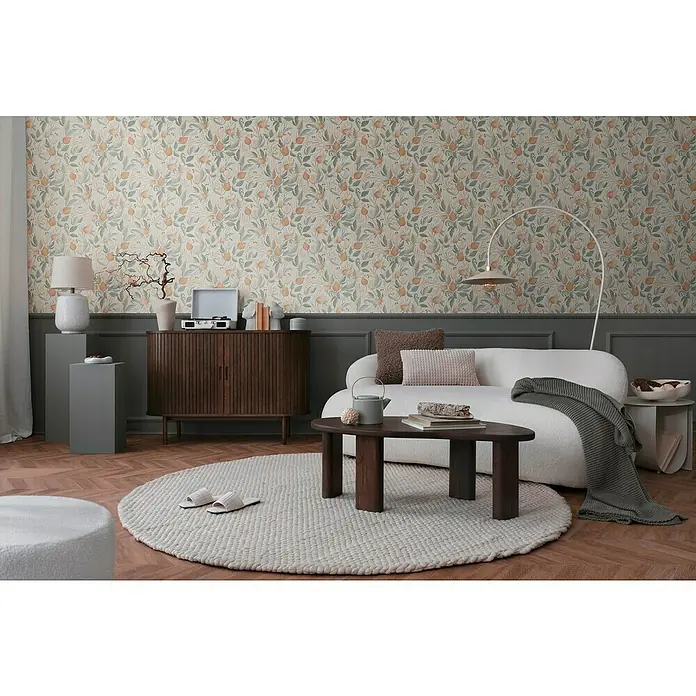 A.S. Création Cosmoliving by Cosmopolitan Vliestapete Blüte - Orange-Creme-Grün, Floral, 10,05 x 0,53 m - Wohnzimmer mit gemusterter Tapete, stilvollem Sofa, Holztisch und rundem Teppich, der eine gemütliche Atmosphäre schafft.