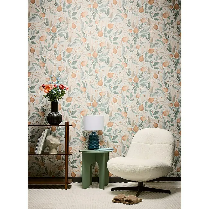 A.S. Création Cosmoliving by Cosmopolitan Vliestapete Blüte - Orange-Creme-Grün, Floral, 10,05 x 0,53 m - Gemütliches Zimmer mit floraler Tapete, weißem Sessel und Holzregal. Die Lampe auf dem grünen Tisch spendet warmes Licht für entspannte Stunden.