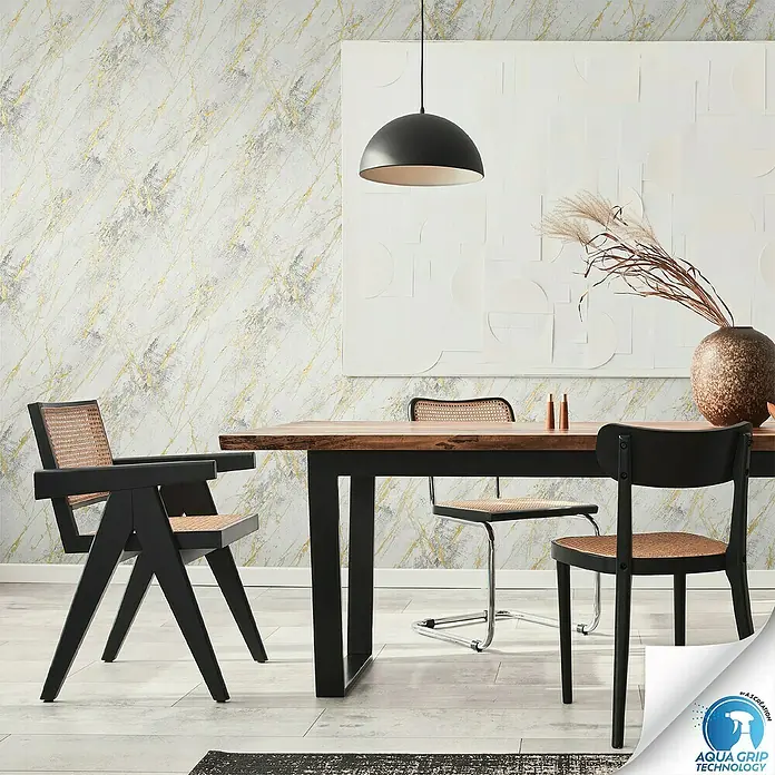 A.S. Création Designdrop Vliestapete Marmoroptik - Weiß-Gold, Steinoptik, 10,05 x 0,53 m - Ein Esszimmer mit einem Holztisch und Stühlen mit Rattan-Sitzen, beleuchtet von einer modernen Pendelleuchte. Die Tapete hat ein Marmormuster.