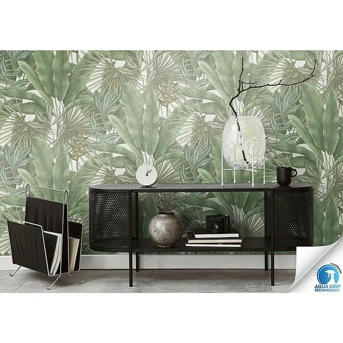 A.S. Création Designdrop Vliestapete Palme - Grün-Beige, Floral, 10,05 x 0,53 m - Produktansicht mit einem schwarzen Konsolentisch, einer Uhr, einer Vase und einem Zeitschriftenständer vor einem tropischen Blättertapetenhintergrund.