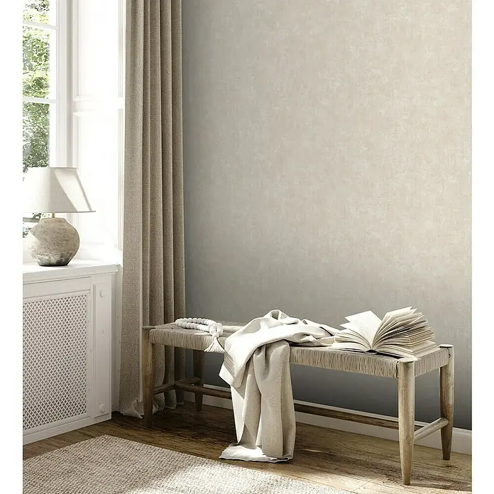 A.S. Création Hygge 3 Vliestapete - Mittelbeige, Uni, 10,05 x 0,53 m - Elegante Szene mit einer schlichten Sitzbank, einem offenen Buch und einer weichen Decke, die eine ruhige und einladende Atmosphäre schafft.
