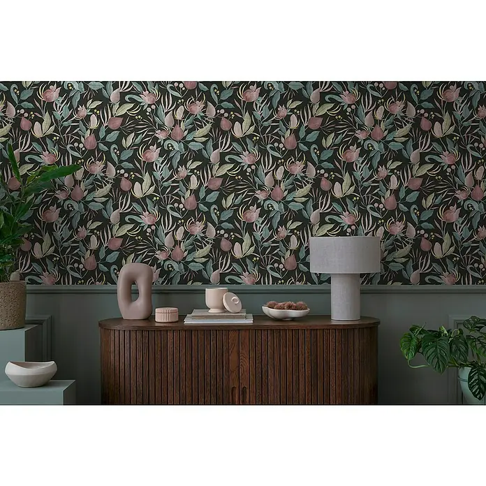 A.S. Création Cosmoliving by Cosmopolitan Vliestapete Blüte - Schwarz-Blau-Pink, Floral, 10,05 x 0,53 m - Dekoratives Interieur mit einer Kommode aus Holz und einer Lampe auf dem Tisch, vor einer floralen Tapete in dunklen Farben.