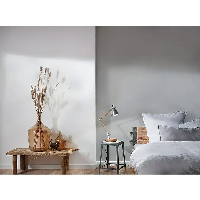 A.S. Création Hygge 3 Vliestapete - Hellgrau II, Uni, 10,05 x 0,53 m - Einrichten mit rustikalem Charme: Eine große Glasvase mit Trockenblumen, neben einer kleineren Flasche und einer Tierfigur auf einem Holztisch.