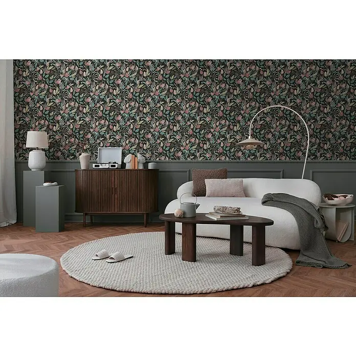 A.S. Création Cosmoliving by Cosmopolitan Vliestapete Blüte - Schwarz-Blau-Pink, Floral, 10,05 x 0,53 m - Ein stilvolles Wohnzimmer mit einem eleganten Sofa und einem dunklen Holztisch auf einem runden Teppich. Die floral gemusterte Tapete sorgt für eine behagliche Atmosphäre.