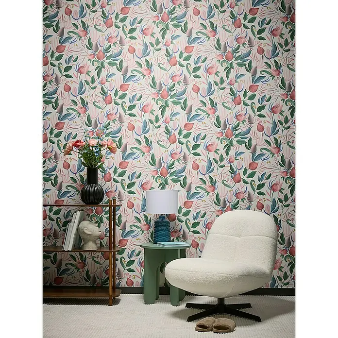 A.S. Création Cosmoliving by Cosmopolitan Vliestapete Blüte - Weiß-Grün-Pink, Floral, 10,05 x 0,53 m - Ein gemütlicher Sessel mit Teddyfellbezug steht vor einer floralen Tapete, kombiniert mit einem Beistelltisch und einem Regal.