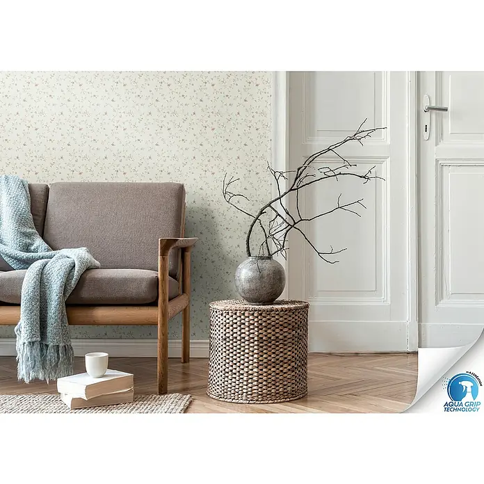 A.S. Création Designdrop Vliestapete Blume - Weiß-Rosa, Floral, 10,05 x 0,53 m - Ein elegantes Wohnzimmer mit einer Couch, einem Beistelltisch mit Vase und zart gemusterter Tapete für ein stilvolles Ambiente.