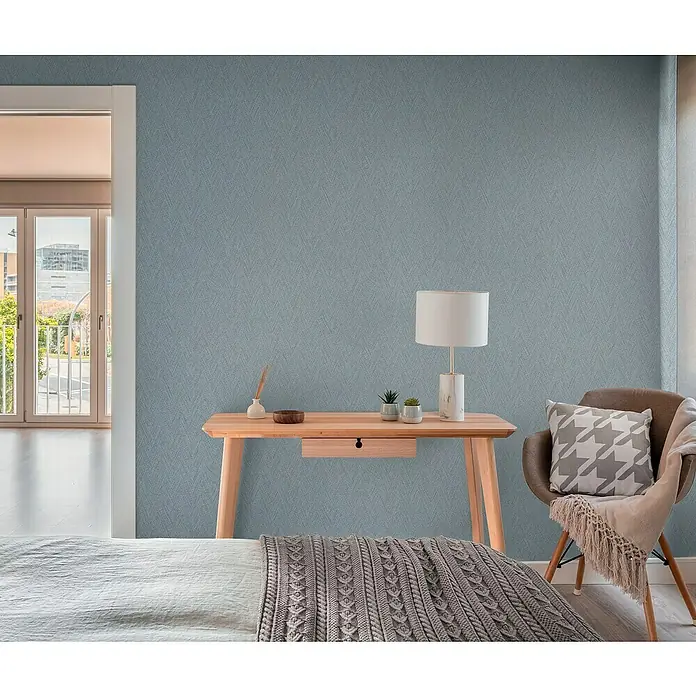 A.S. Création Hygge 3 Vliestapete - Grau-Blau, Uni, 10,05 x 0,53 m - Einladendes Schlafzimmer mit stilvollem Schreibtisch, Lampe und Stuhl vor einer gemusterten blauen Wandtapete.
