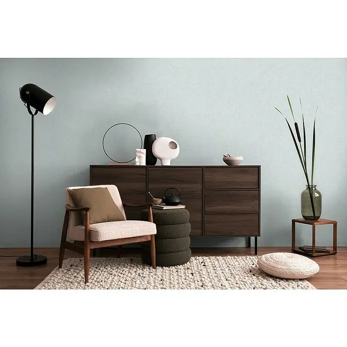A.S. Création Cosmoliving by Cosmopolitan Vliestapete - Pastellblau, Uni, 10,05 x 0,53 m - Elegantes Wohnzimmer mit stilvollem Sideboard aus dunklem Holz, ergänzt durch einen Akzentstuhl, eine Stehlampe und dekorative Accessoires.