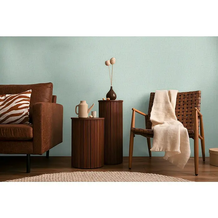 A.S. Création Cosmoliving by Cosmopolitan Vliestapete - Türkis meliert, Uni, 10,05 x 0,53 m - Wohnzimmer mit braunem Ledersofa, zwei Beistelltischen und einem geflochtenen Sessel mit Decke. Die Wände sind hellblau.