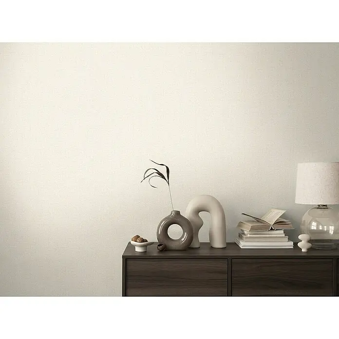 A.S. Création Cosmoliving by Cosmopolitan Vliestapete - Hell-Beige, Uni, 10,05 x 0,53 m - Elegant arrangierte Wohnaccessoires auf einer dunklen Holzkommode, inklusive Lampe, Bücher und dekorativer Vasen.