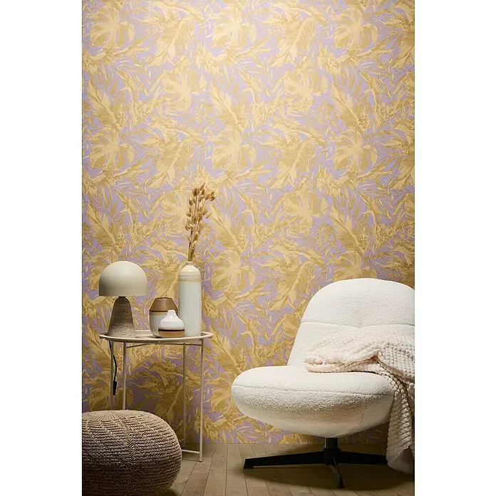 A.S. Création Cosmoliving by Cosmopolitan Vliestapete Blätter - Lila-Gold-Braun, Floral, 10,05 x 0,53 m - Elegante Inneneinrichtung mit einem weißen Sessel, einem Beistelltisch mit Lampe und Vasen vor einer floral gemusterten Tapete in Gold und Lila.