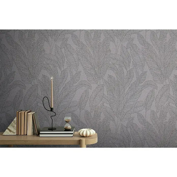 A.S. Création Cosmoliving by Cosmopolitan Vliestapete Blätter - Grau-Schwarz, Floral, 10,05 x 0,53 m - Nahaufnahme eines Raumes mit grauer Tapete mit Blätter-Muster und einem Tisch mit dekorativen Elementen wie Kerzen und Büchern.