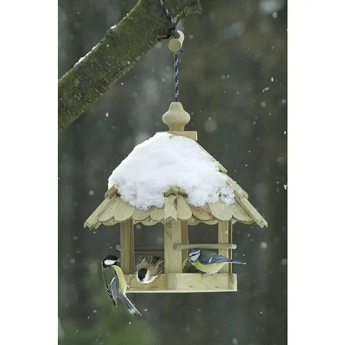 Dobar Sechseck-Vogelfutterhaus - Hellbraun, 35 x 31 x 37 cm - Ein mit Schnee bedecktes Vogelhaus, an dem drei kleine Vögel fressen. Toller Artikel für die Vogelfütterung im Winter.