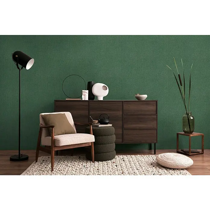 A.S. Création Cosmoliving by Cosmopolitan Vliestapete - Grün meliert, Uni, 10,05 x 0,53 m - Das Bild zeigt ein modernes Wohnzimmer mit einem braunen Sideboard, einem bequemen Sessel und einer stilvollen Stehlampe.