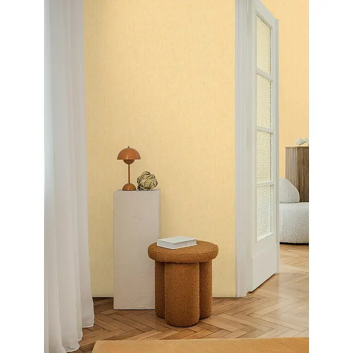 A.S. Création Cosmoliving by Cosmopolitan Vliestapete - Gelb, Uni, 10,05 x 0,53 m - Elegantes Interieur mit beigem Hocker, minimalistischem Tisch und einer dekorativen Lampe, die eine warme Atmosphäre schafft.