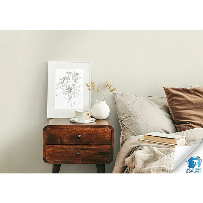 A.S. Création Designdrop Vliestapete - Beige, Uni, 10,05 x 0,53 m - Nahaufnahme eines Nachttisches aus Holz mit zwei Schubladen, darauf ein Bild, eine Tasse und eine Vase mit Trockenblumen.