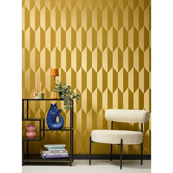 A.S. Création Cosmoliving by Cosmopolitan Vliestapete 3D-Grafik - Gold-Metallic-Gelb, Grafisch, 10,05 x 0,53 m - Nahaufnahme eines Zimmers mit einer eleganten Sitzgelegenheit und einem Regal vor einer goldenen geometrischen Tapete.