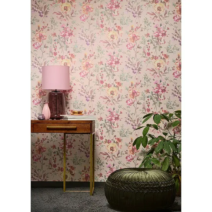 A.S. Création Cosmoliving by Cosmopolitan Vliestapete Blüten - Rosa-Metallic-Grün, Floral, 10,05 x 0,53 m - Nahaufnahme eines Raumes mit einem eleganten Schreibtisch, einer stilvollen Lampe und einem dekorativen Puff vor einer floralen Tapete.