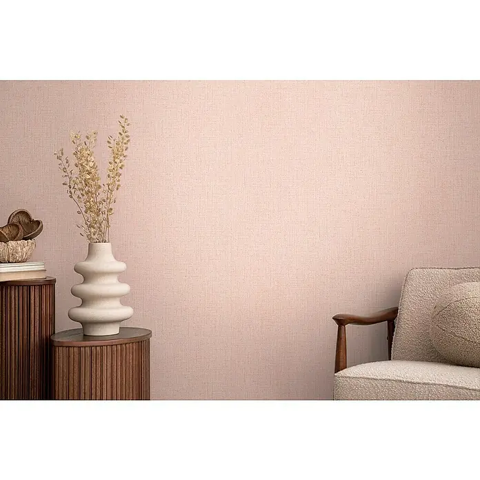 A.S. Création Cosmoliving by Cosmopolitan Vliestapete - Rosa meliert, Uni, 10,05 x 0,53 m - Dekoratives Stillleben mit einer skulpturalen Vase auf einem Holzschrank, daneben ein bequemer Sessel vor einer strukturierten rosa Wand.