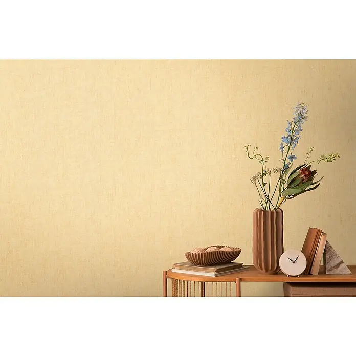A.S. Création Cosmoliving by Cosmopolitan Vliestapete - Gelb, Uni, 10,05 x 0,53 m - Stillleben mit Vase, Blumen, Büchern und Uhr auf einem Tisch. Eine dekorative Anordnung in warmen Farbtönen vor einem beigen Hintergrund.