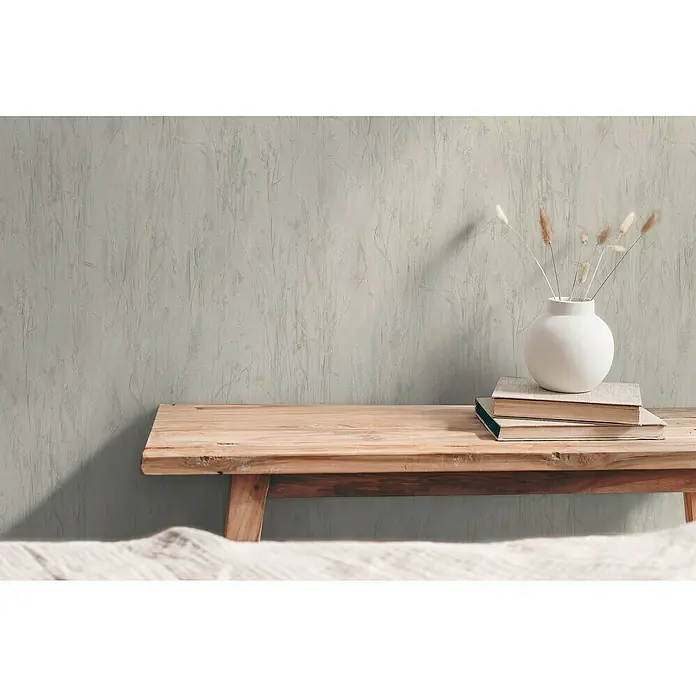 A.S. Création Hygge 3 Vliestapete Floral - Grau, Floral, 10,05 x 0,53 m - Eine weiße Vase mit Trockenblumen auf einem Stapel Bücher, platziert auf einer hölzernen Bank vor einer strukturierten Wand.
