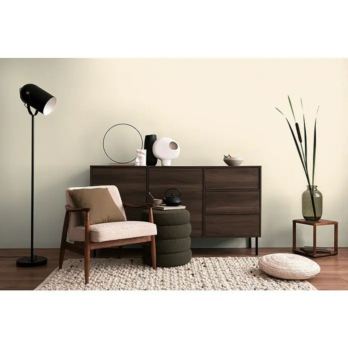 A.S. Création Cosmoliving by Cosmopolitan Vliestapete - Hellcreme, Uni, 10,05 x 0,53 m - Einladendes Interieur mit einem stilvollen Sessel mit Kissen auf einem Teppich, ergänzt durch eine Stehlampe und eine Kommode.