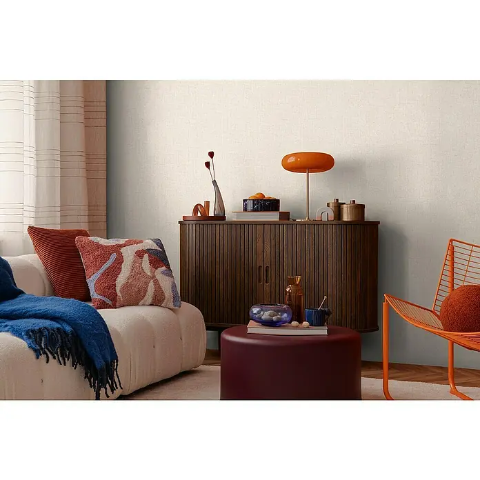 A.S. Création Cosmoliving by Cosmopolitan Vliestapete - Helles Cremebeige, Uni, 10,05 x 0,53 m - Einrichtungsidee mit einem stilvollen Holzschrank, einem bequemen Sofa mit Kissen und einer modernen Lampe, die eine warme und einladende Atmosphäre schaffen.