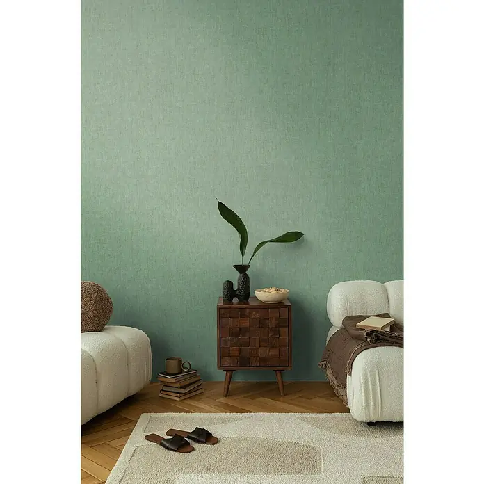 A.S. Création Cosmoliving by Cosmopolitan Vliestapete - Grün, Uni, 10,05 x 0,53 m - Ein stilvolles Interieur mit einem Holztisch, Pflanzen, bequemen Sesseln und einem Teppich, der eine warme und einladende Atmosphäre schafft.
