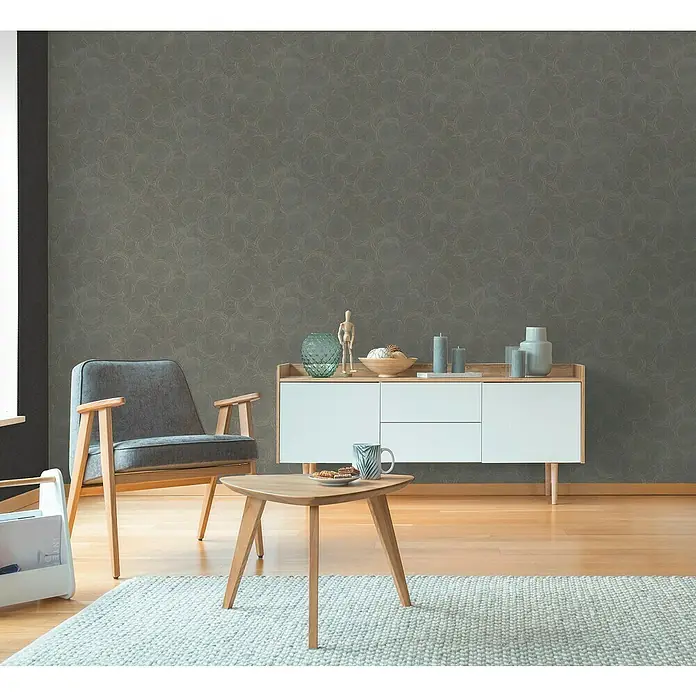 A.S. Création Hygge 3 Vliestapete Kreise - Grau-Braun, Grafisch, 10,05 x 0,53 m - Einrichtungsidee mit modernem grauen Sessel, hellbraunem Tisch und weißem Sideboard vor einer grauen gemusterten Tapete.