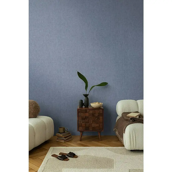 A.S. Création Cosmoliving by Cosmopolitan Vliestapete - Mittelblau, Uni, 10,05 x 0,53 m - Innenaufnahme eines Wohnzimmers mit hellen Sesseln, Holzboden und einem kleinen Schrank mit Dekoration.