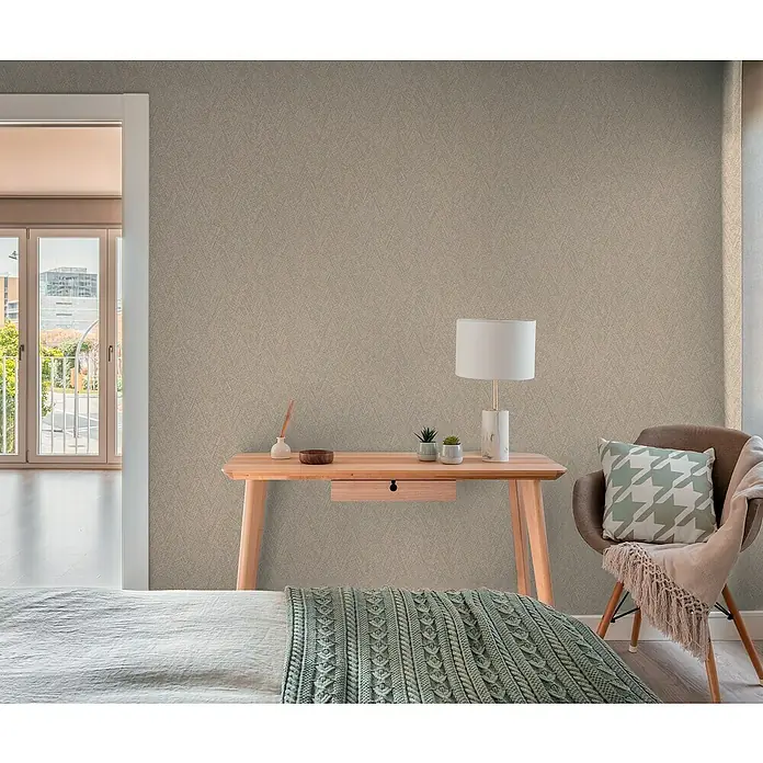 A.S. Création Hygge 3 Vliestapete - Braun, Uni, 10,05 x 0,53 m - Einladendes Interieur mit einem hellen Holztisch, einer Lampe und einem Sessel mit Kissen, das ein gemütliches Ambiente schafft.