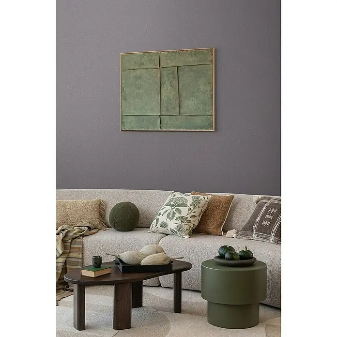 A.S. Création Cosmoliving by Cosmopolitan Vliestapete - Dunkelgrau, Uni, 10,05 x 0,53 m - Wohnzimmer mit Couch, Kissen und Kunstwerk an der Wand. Der Raum strahlt Gemütlichkeit aus.