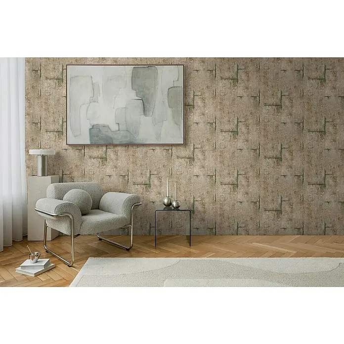A.S. Création Cosmoliving by Cosmopolitan Vliestapete Beton - Braun-Grau-Grün, Betonoptik, 10,05 x 0,53 m - Ein grauer Sessel mit silbernen Akzenten steht vor einer Wand mit abstraktem Gemälde und einer Tischlampe.