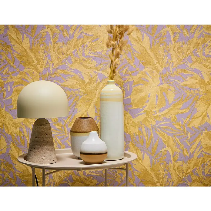 A.S. Création Cosmoliving by Cosmopolitan Vliestapete Blätter - Lila-Gold-Braun, Floral, 10,05 x 0,53 m - Nahaufnahme eines Tisches mit einer Lampe und Vasen, vor einer Wand mit Blattmuster.