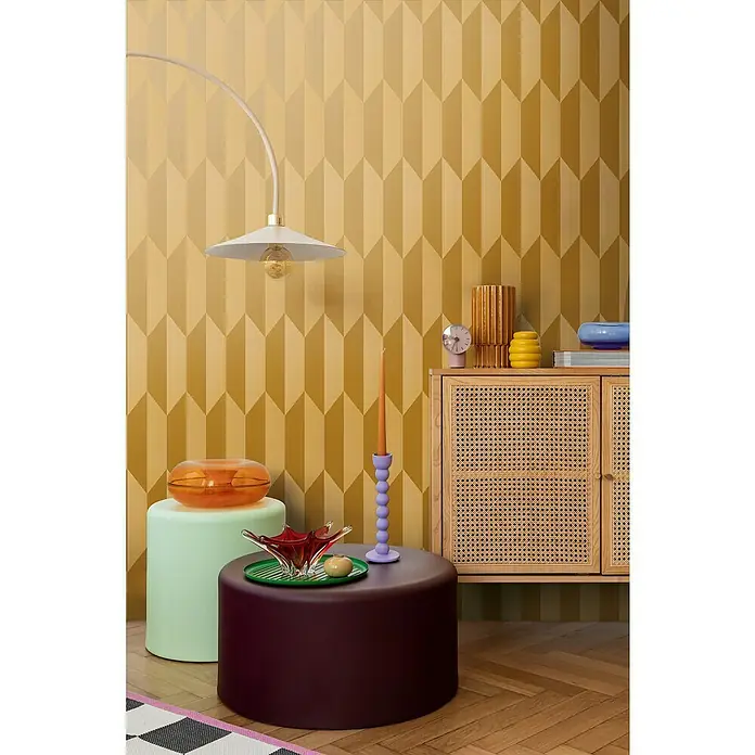 A.S. Création Cosmoliving by Cosmopolitan Vliestapete 3D-Grafik - Gold-Metallic-Gelb, Grafisch, 10,05 x 0,53 m - Wohnzimmer-Szene mit auffälligen Möbeln und dekorativen Elementen auf einem gepflegten Holzboden vor einer geometrischen Wand.