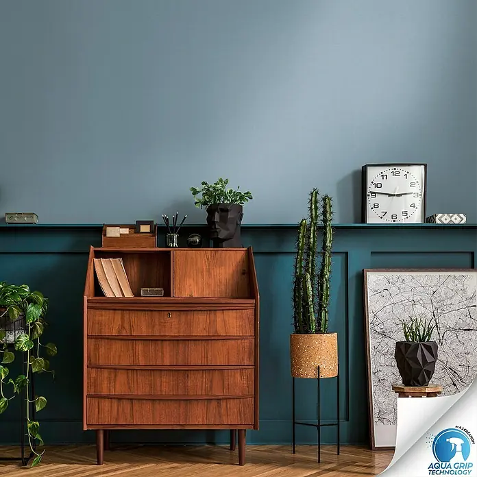 A.S. Création Designdrop Vliestapete - Blau, Uni, 10,05 x 0,53 m - Elegante Inneneinrichtung mit einem dunklen Holzschreibtisch, umgeben von Pflanzen, die eine warme, einladende Atmosphäre schaffen.