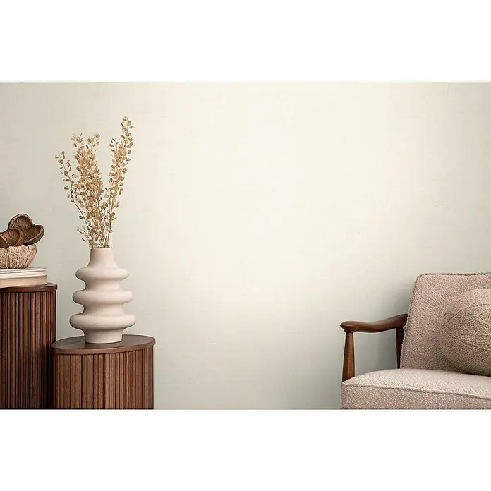 A.S. Création Cosmoliving by Cosmopolitan Vliestapete - Hellbeige, Uni, 10,05 x 0,53 m - Einrichten mit einer modernen Vase auf einem Holzschrank und einem Sessel mit Kissen vor einer hellen Wand für ein stilvolles Ambiente.