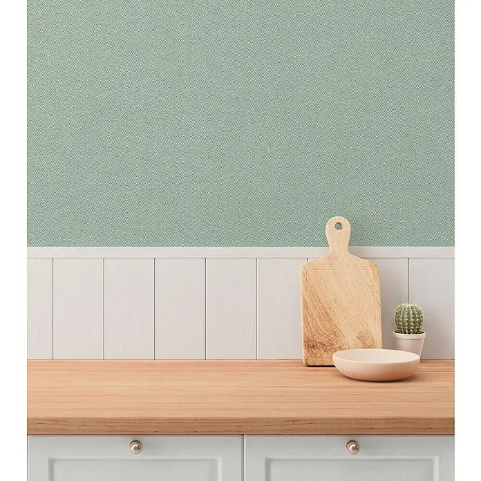 A.S. Création Hygge 3 Vliestapete - Mittelgrün, Uni, 10,05 x 0,53 m - Rustikale Küche mit Schneidebrett und Schüssel aus Holz auf einer hellen Arbeitsplatte vor einer weißen Paneelwand und mintgrüner Tapete.