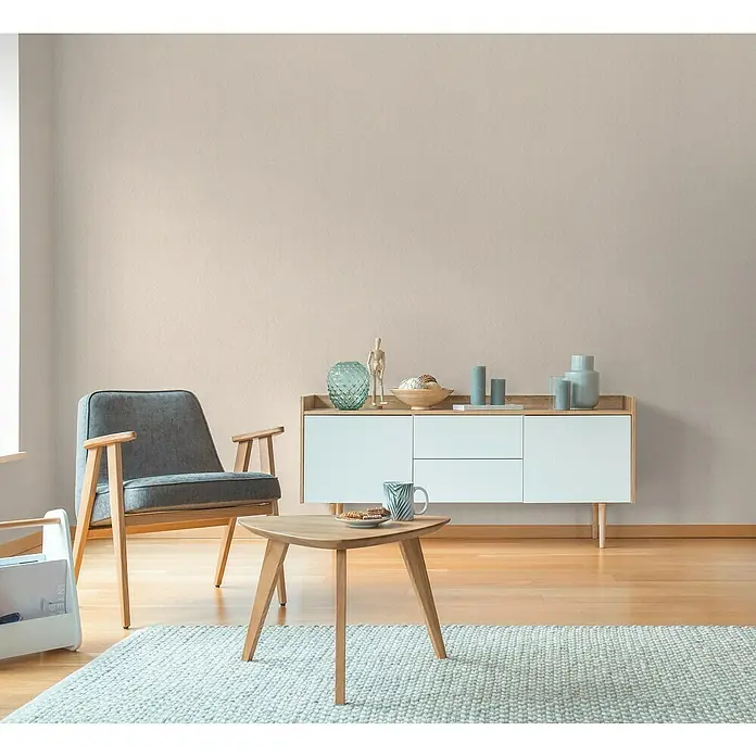 A.S. Création Hygge 3 Vliestapete - Beigebraun, Uni, 10,05 x 0,53 m - Helle Inneneinrichtung mit modernem Sideboard, einem Sessel und einem kleinen Tisch auf einem hellen Teppich. Elegantes Wohnambiente.