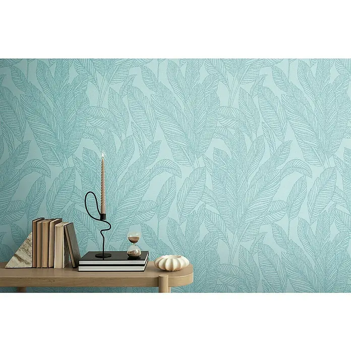 A.S. Création Cosmoliving by Cosmopolitan Vliestapete Blätter - Blau-Gold, Floral, 10,05 x 0,53 m - Nahaufnahme einer stilvollen Tischdekoration mit Kerze, Büchern und Sanduhr vor einer blauen Blättertapete.