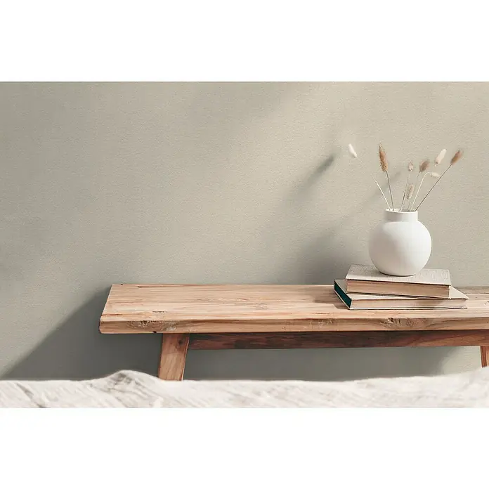 A.S. Création Hygge 3 Vliestapete - Grau-Beige, Uni, 10,05 x 0,53 m - Stillleben mit einer weißen Vase auf Büchern auf einer Holzbank vor einer hellen Wand, minimalistisch und ruhig.