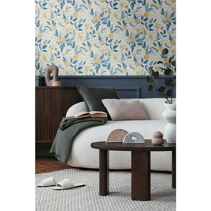 A.S. Création Cosmoliving by Cosmopolitan Vliestapete Blüte - Weiß-Blau-Gelb, Floral, 10,05 x 0,53 m - Nahaufnahme eines elegant eingerichteten Wohnzimmers mit floraler Tapete, Sofa, Holztisch und dekorativen Accessoires.