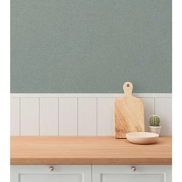 A.S. Création Hygge 3 Vliestapete - Pastellgrün, Uni, 10,05 x 0,53 m - Küchentisch mit Schneidebrett, Schale und Kaktus vor einer Wand mit Holzvertäfelung und blaugrüner Tapete.