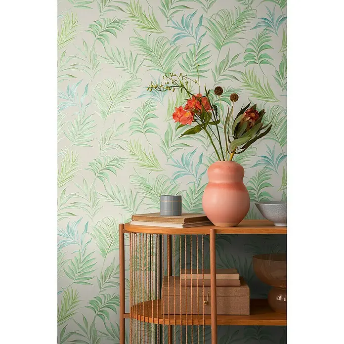 A.S. Création Cosmoliving by Cosmopolitan Vliestapete Ranken - Weiß-Grün-Blau, Floral, 10,05 x 0,53 m - Elegantes Regal aus Holz mit dekorativen Accessoires wie Vasen, Büchern und Schachteln, vor einer Wand mit tropischem Blättermuster.