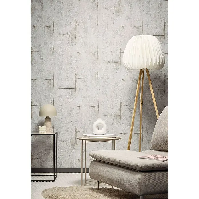 A.S. Création Cosmoliving by Cosmopolitan Vliestapete Beton - Grau-Braun, Betonoptik, 10,05 x 0,53 m - Einrichten mit Stil: Wandtapete im Beton-Look, ergänzt durch eine Stehlampe mit Stoffschirm und einen Sessel in harmonischen Farbtönen.