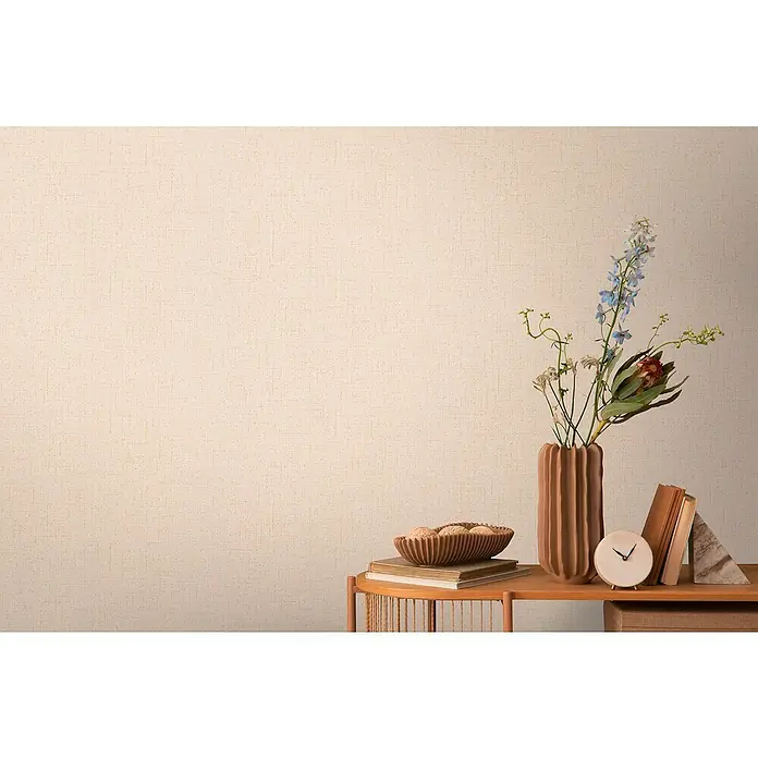 A.S. Création Cosmoliving by Cosmopolitan Vliestapete - Mittelbeige, Uni, 10,05 x 0,53 m - Nahaufnahme eines dekorierten Tisches mit einer Vase, Büchern, einer Schale und einer Uhr, die das Wohnambiente hervorheben.