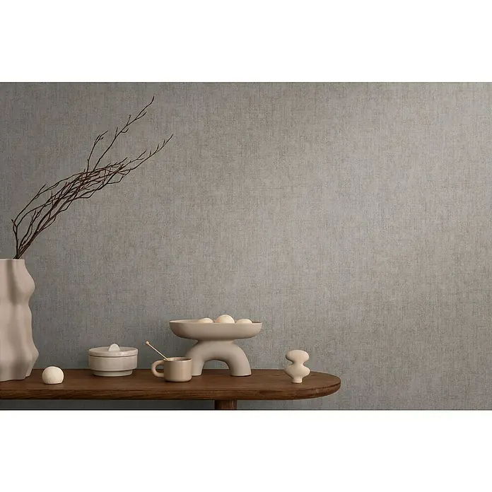 A.S. Création Cosmoliving by Cosmopolitan Vliestapete - Grau, Uni, 10,05 x 0,53 m - Stillleben mit einer Vase, einer Schale mit Kugeln, einer Dose und einer Tasse auf einem Holztisch vor einer grauen Wand.