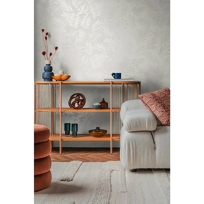 A.S. Création Cosmoliving by Cosmopolitan Vliestapete Ranken - Weiß-Creme, Floral, 10,05 x 0,53 m - Nahaufnahme eines Regals mit Dekorationsgegenständen und einem cremefarbenen Sessel vor einer eleganten, gemusterten Tapete.