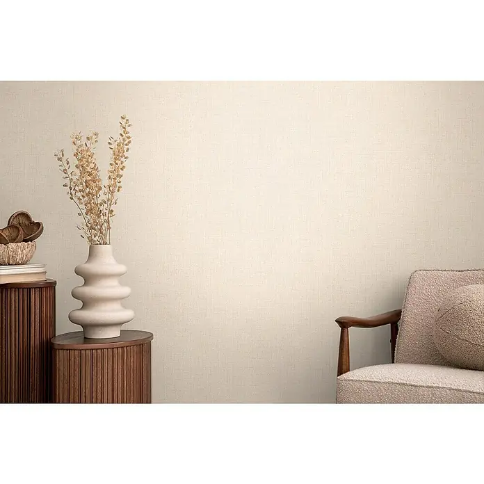 A.S. Création Cosmoliving by Cosmopolitan Vliestapete - Beige I, Uni, 10,05 x 0,53 m - Einrichtungsfoto mit einer hellen, bauchigen Vase mit Trockenblumen auf einem kleinen Schrank neben einem Sessel.